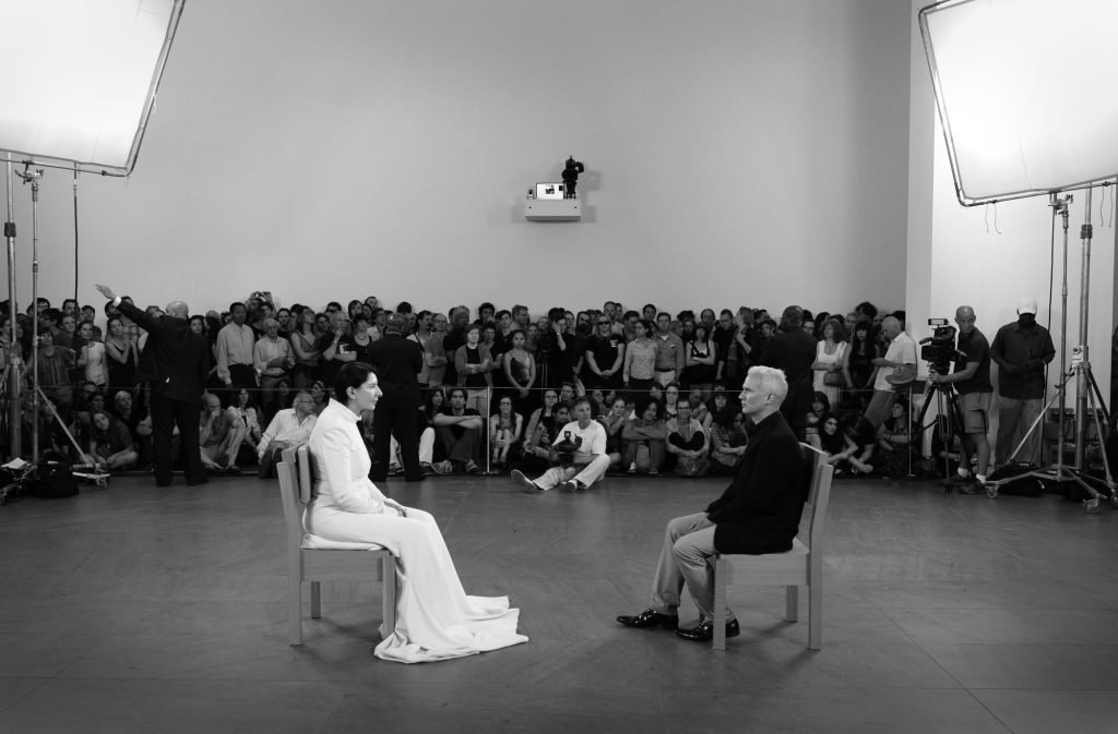 Marina Abramović, {{The Artist is Present}} uit 2010, is waarschijnlijk de bekendste performance van Abramović. In het MoMA in New York zat ze op een stoel en konden bezoekers één voor één tegenover haar plaatsnemen, om elkaar vervolgens zwijgend aan te kijken. De tentoonstelling werd door 750.000 mensen bezocht. Foto: Marco Anelli, courtesy Marina Abramović Archives